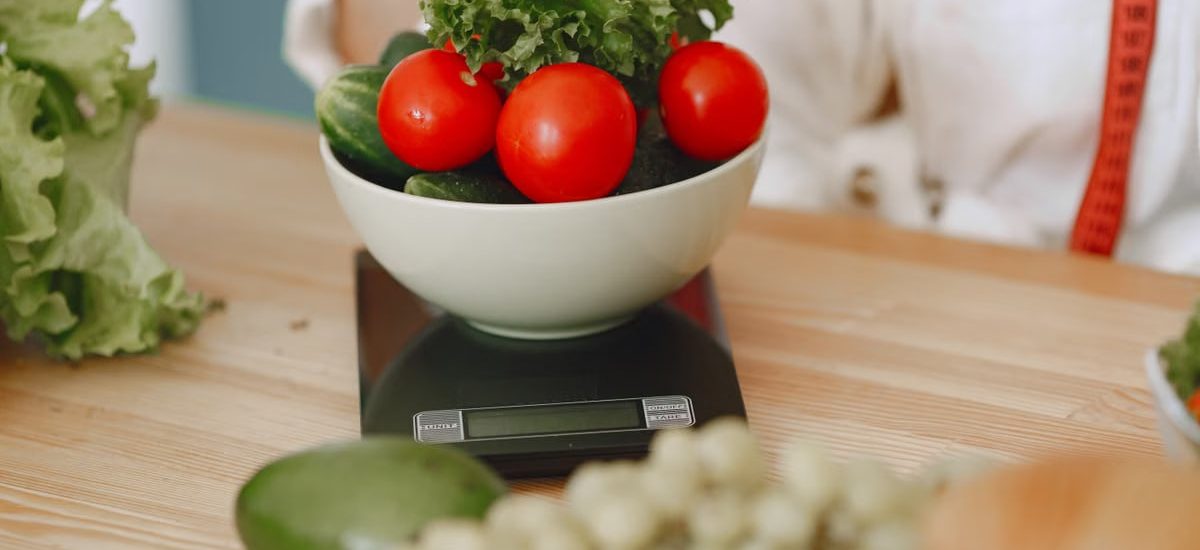 Colorful fresh vegetables including tomatoes and cucumbers on a kitchen scale for healthy eating.
