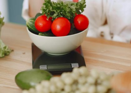 Colorful fresh vegetables including tomatoes and cucumbers on a kitchen scale for healthy eating.
