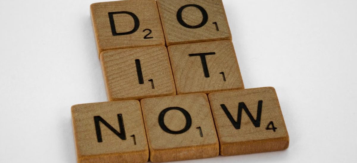 Wooden scrabble tiles forming 'DO IT NOW' on a minimal white backdrop. Inspiring concept.