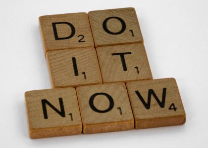 Wooden scrabble tiles forming 'DO IT NOW' on a minimal white backdrop. Inspiring concept.